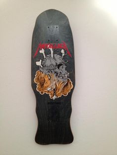 a skateboard that has been painted with metallic skulls and bones on it, hanging up against a white wall