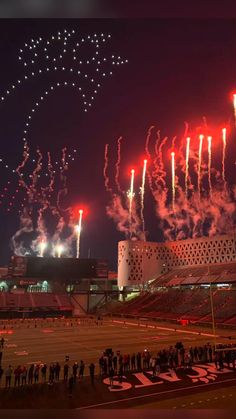 fireworks are lit up in the night sky over an empty football stadium as people watch