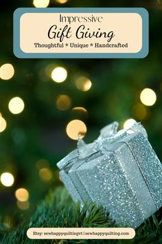 a silver gift box sitting on top of a christmas tree with lights in the background