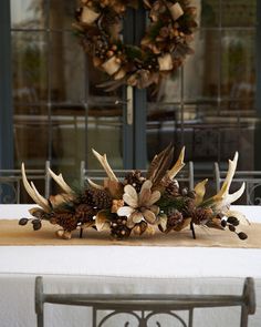 a wreath with antlers and pine cones sits on a table in front of a window