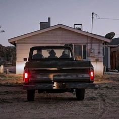 two people in the back of a pick - up truck parked outside a small house