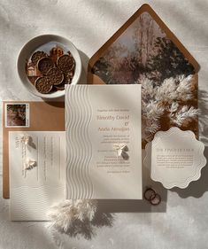 an assortment of wedding stationery items on top of a white table cloth with a bowl of cookies