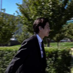 a man in a suit and tie is walking down the street with trees behind him