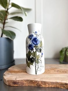 a blue and white vase sitting on top of a wooden board next to a potted plant