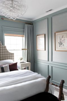 a bedroom with blue walls, white bedding and a chandelier hanging from the ceiling