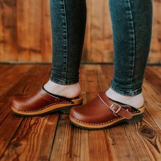 Experience Unmatched Comfort and Style;  Brown Wooden Clogs crafted from natural cowhide leather, our 2mm-thick brown colored clogs redefine comfort and elegance. The addition of an adjustable strap with a buckle ensures a snug fit, eliminating worries about fastening length. Glide through your day with ease, knowing these wooden shoes provide the perfect balance of support and flexibility. Premium Material, Superior Quality;  Step into luxury with our closed toe wooden clogs, meticulously designed for both clogs men and clogs women. The durable upper crafted from natural cowhide leather promises longevity, while the real wood and PU rubber bottom offer stability without the traditional clacking sound. Elevate your footwear collection with these premium, versatile clogs. Unleash Your Style Brown Clogs, Swedish Clogs, Clogs And Mules, Wooden Clogs, Alder Wood, Wooden Shoes, Clogs Shoes, Womens Clogs, Natural Leather