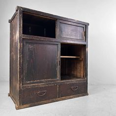 an old wooden cabinet with two drawers and one door open on the bottom shelf, in front of a white wall