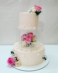 a three tiered cake with pink and white flowers on the top, sitting on a plate