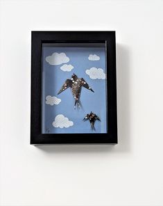 two birds are flying through the sky in a shadow box with paper clouds behind them