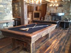 a pool table in the middle of a room with wood flooring and stone fireplace