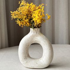 a white vase filled with yellow flowers sitting on top of a table next to a curtain