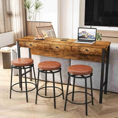 three stools are sitting in front of a wooden table with drawers and a laptop on it