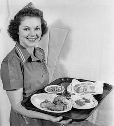 an old photo of a woman holding a tray full of food and smiling at the camera