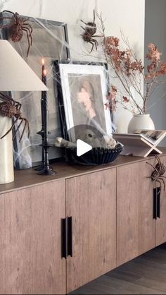 a wooden cabinet with pictures and candles on it in front of a wall decorated with spider webs