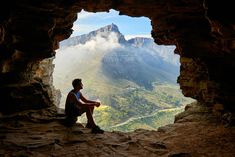 a man sitting on the edge of a cliff looking out at mountains and valley below