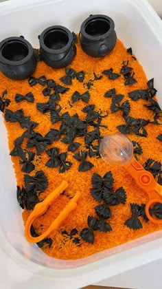 a plastic container filled with orange rice and black flowers on top of it next to scissors