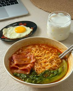 a bowl of ramen with bacon, spinach and eggs next to a glass of milk