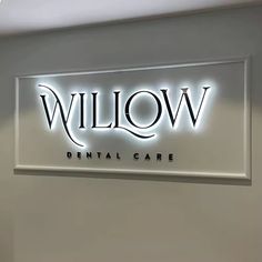 the sign for willow dental care is lit up in front of a wall mounted mirror