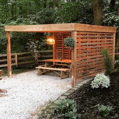 a small wooden shelter in the middle of a park with benches and trees around it