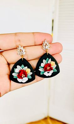 a pair of black and red flower earrings on someone's left hand in front of a white door