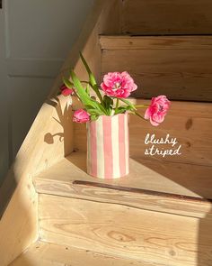 pink flowers sit in a striped vase on the steps leading up to an upstairs stairway