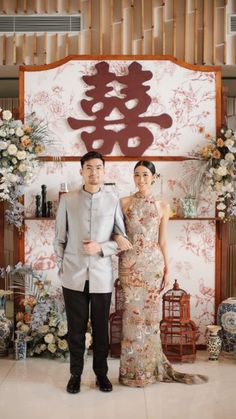 a man and woman standing next to each other in front of a wall with flowers