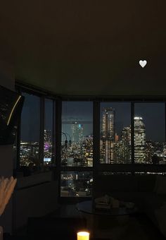 a living room filled with furniture and a large window overlooking the city at night time