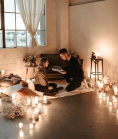 a man and woman sitting on the floor in front of candles with one person reading