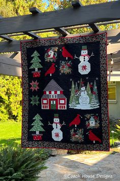 a quilted christmas scene hanging from a pergolated trellis in front of a house