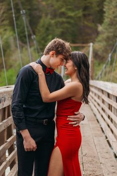 a young man and woman standing on a bridge with their arms around each other as they look into each others eyes