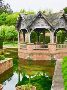 a gazebo in the middle of a pond surrounded by greenery and trees with potted plants on either side