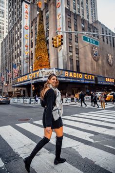 a woman is crossing the street in front of radio city music hall and christmas tree