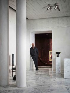 a man leaning against the wall in an empty room with columns and paintings on the walls