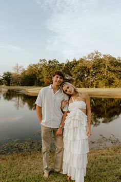 a man and woman standing next to each other in front of a lake