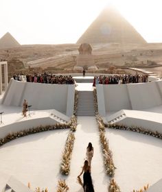 two women are walking towards the pyramids in front of an event with other people