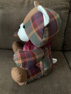 a teddy bear sitting on top of a couch wearing a plaid suit and holding its paws up