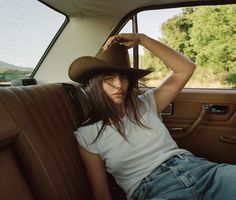 a woman sitting in the back seat of a car wearing a cowboy hat and jeans