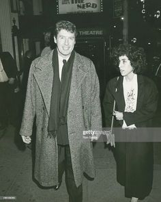 an old black and white photo of a man and woman walking down the street at night