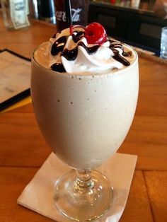 an ice cream sundae with whipped cream and cherries in a glass on a wooden table