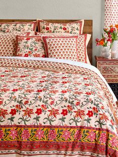 a bed with red and yellow flowers on the comforter is next to a night stand