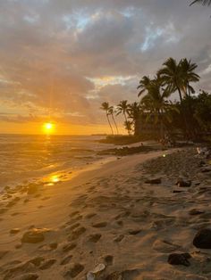 the sun is setting on the beach with palm trees in the foreground and footprints in the sand