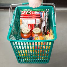 a person is holding a shopping basket full of food and condiments in it