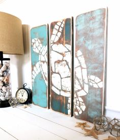 three wooden panels with sea turtles painted on them next to a lamp and clock in front of a window