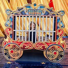 an elaborately painted cart with wheels on display at a carnival or fair, in front of curtained yellow drapes