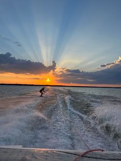 the sun is setting over the water as a wake boarder glides behind him