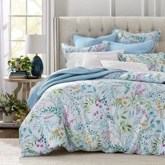 a bed with blue and white comforters in a bedroom next to a window filled with potted plants