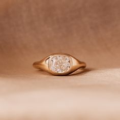 a gold ring with a white diamond in the center on a brown cloth covered surface