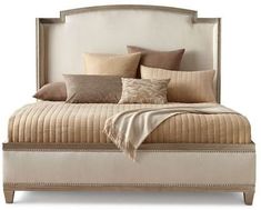 a large bed with pillows and blankets on it's headboard, sitting in front of a white wall