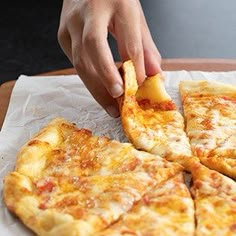 a person taking a slice of cheese pizza from a wooden cutting board on top of a table