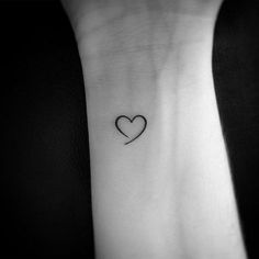 a small heart tattoo on the wrist is shown in black and white, with an arrow